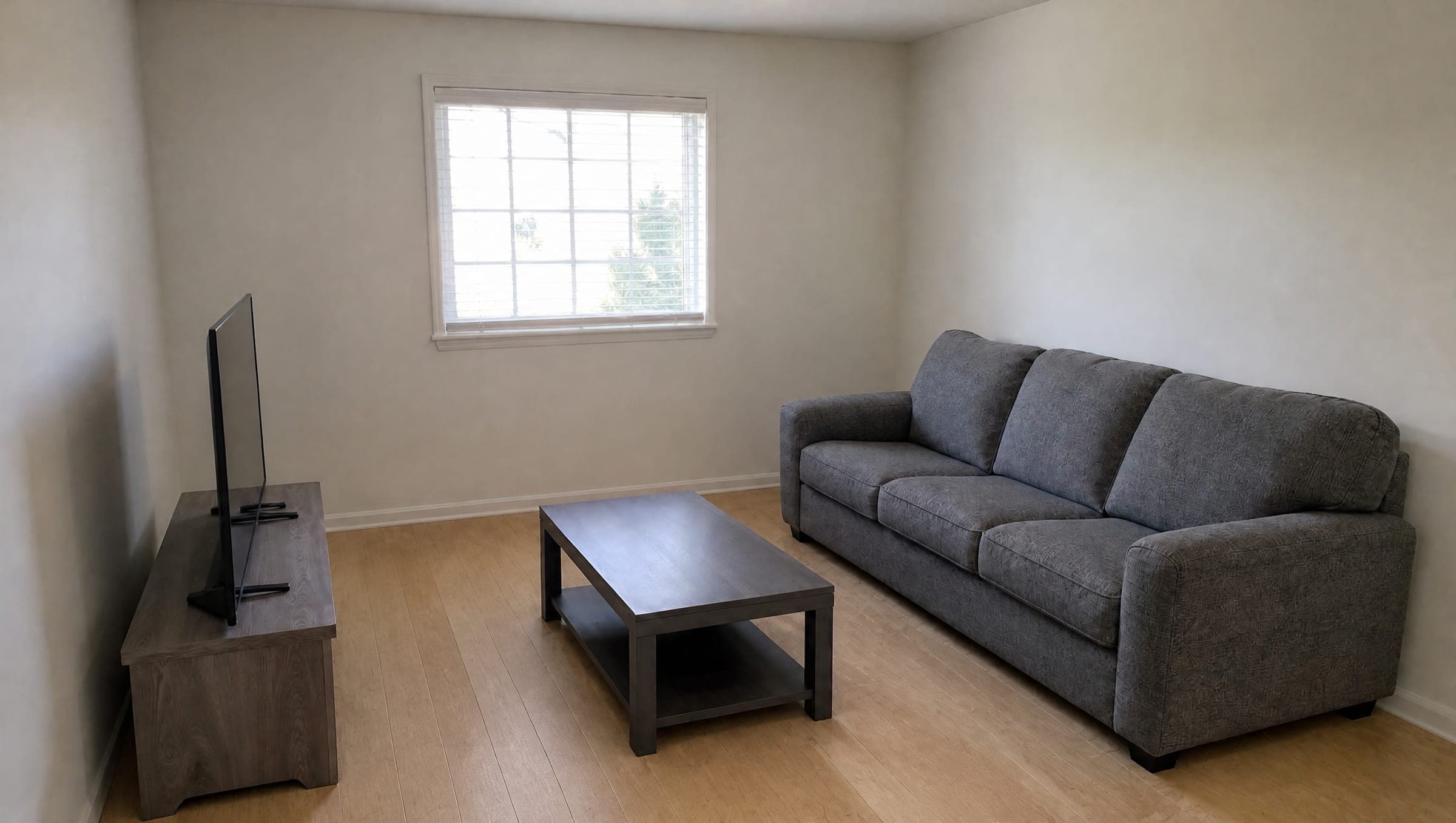 A plain living room with white walls, a grey sofa, a basic coffee table and a light oak floor