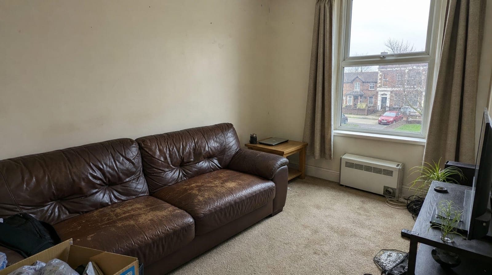 A dull living room with a worn brown leather sofa and beige carpet